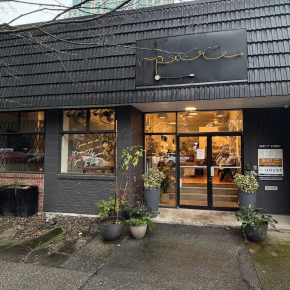 Street-level exterior of commercial retail property at 153 East 1st Street, North Vancouver, featuring dark shingle façade, large display windows with handwritten signage, glass entrance doors.