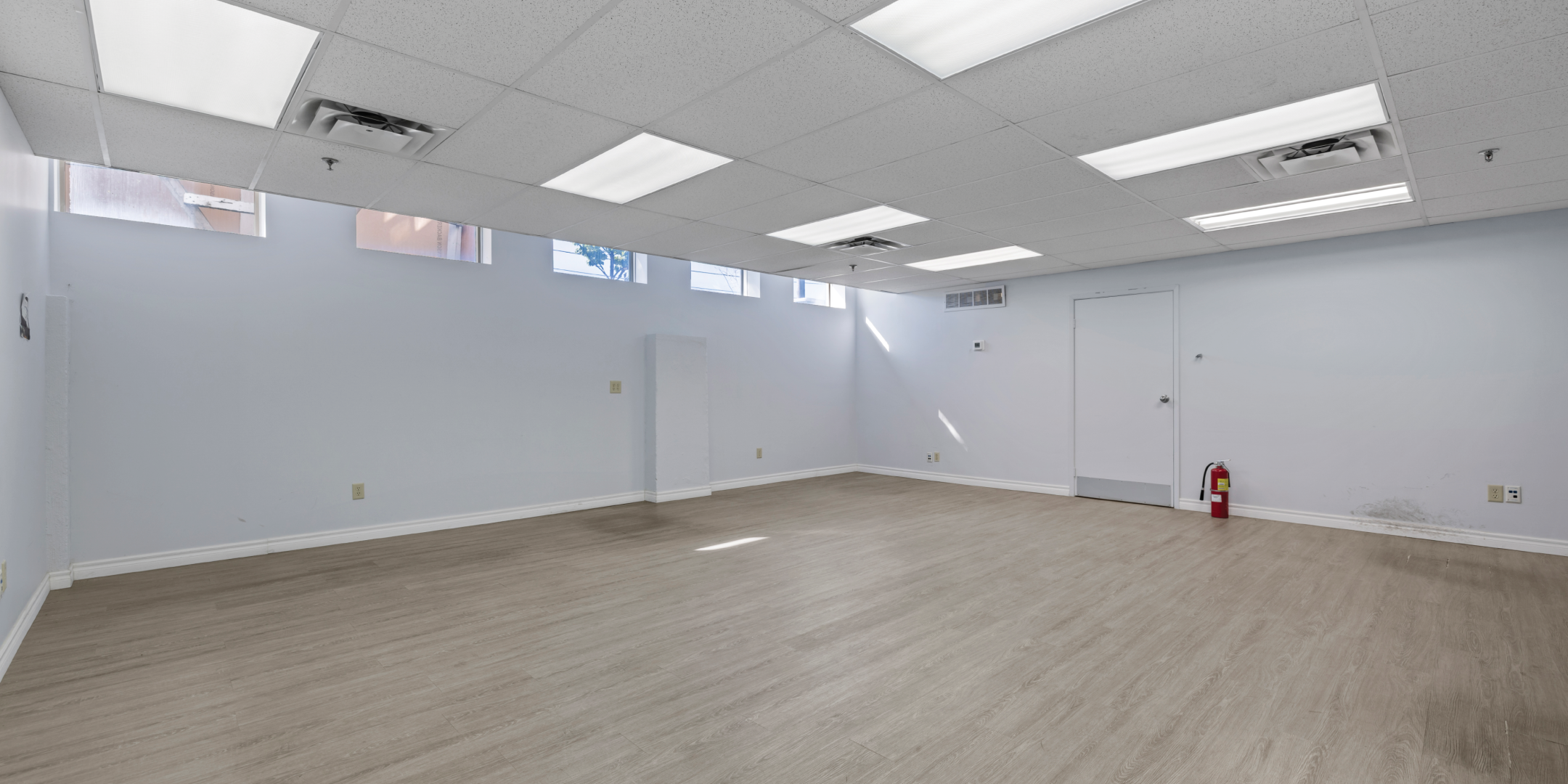3636 Weston Road office with white walls, light wood floors, and suspended ceiling and windows along top of far wall 