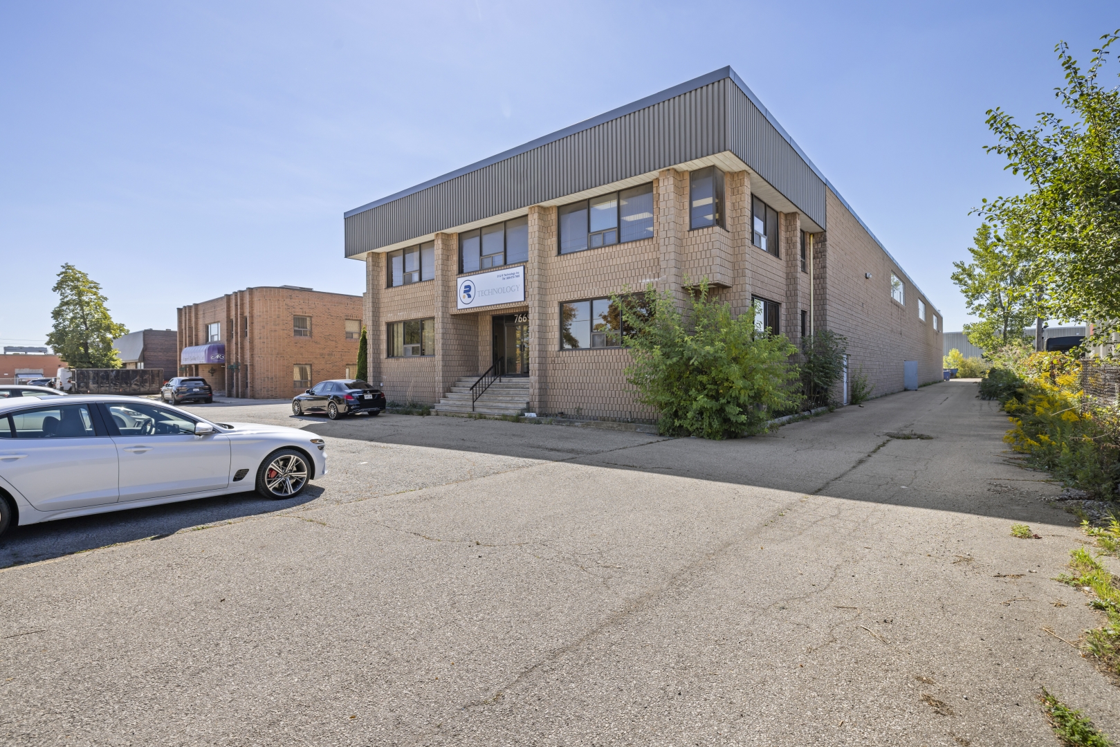 7669 Kimbel Street front view of two storey brick building with driveway down the side and a parking lot in front 