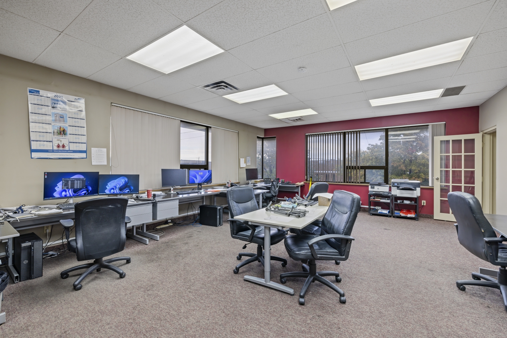 7669 Kimbel Street office with carpet floors, suspended ceiling, windows and desks and chairs along the far wall 
