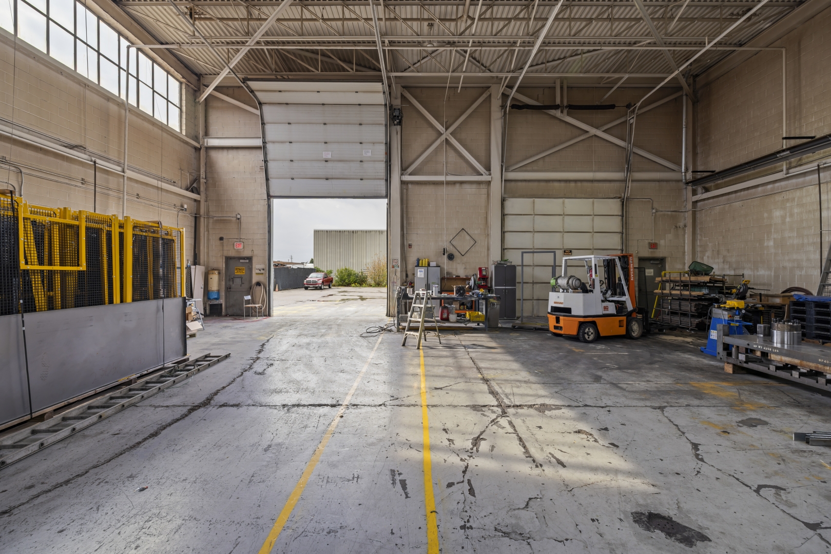 7669 Kimbel Street interior view of shipping doors, concrete floors and windows along the top edge of the wall. One open drive in door, and one closed truck level 