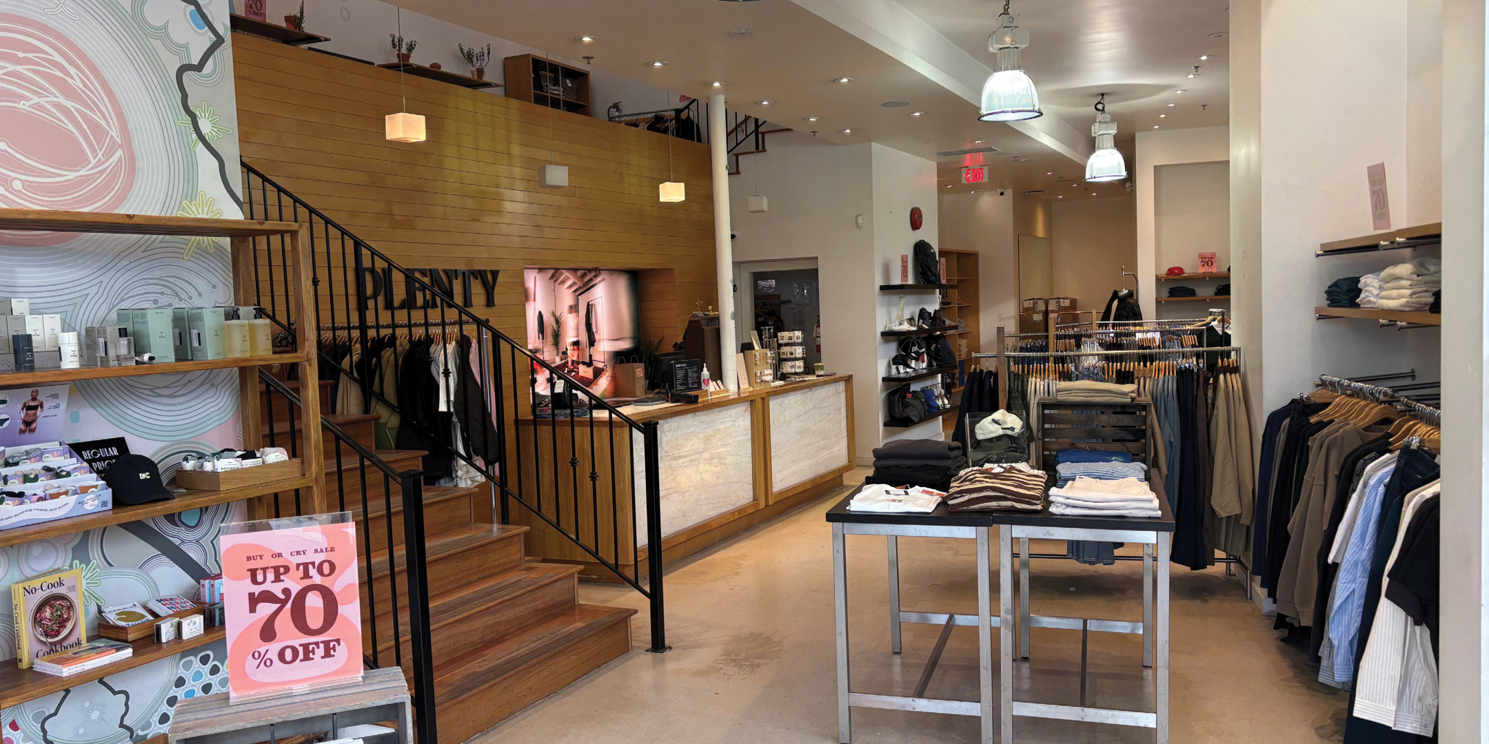 Interior of fashion retail store with clothing on racks and tables with light wood floors and medium wood accents