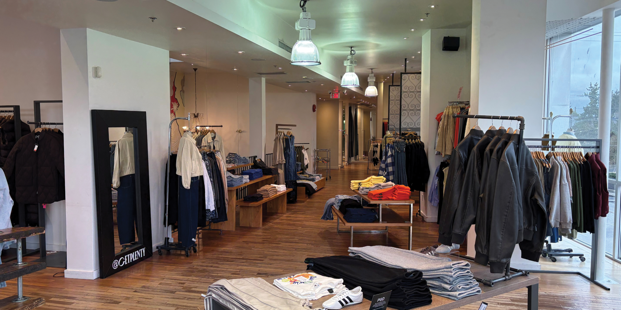 Interior of fashion retail store with clothing on racks and tables with light wood floors and white walls