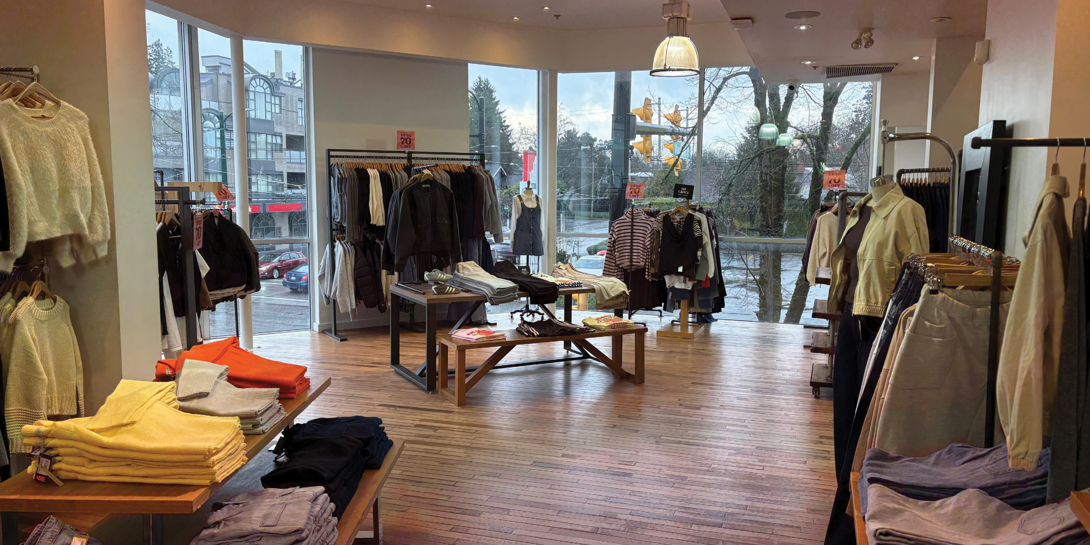 Interior of fashion retail store with clothing on racks and tables with light wood floors and white walls