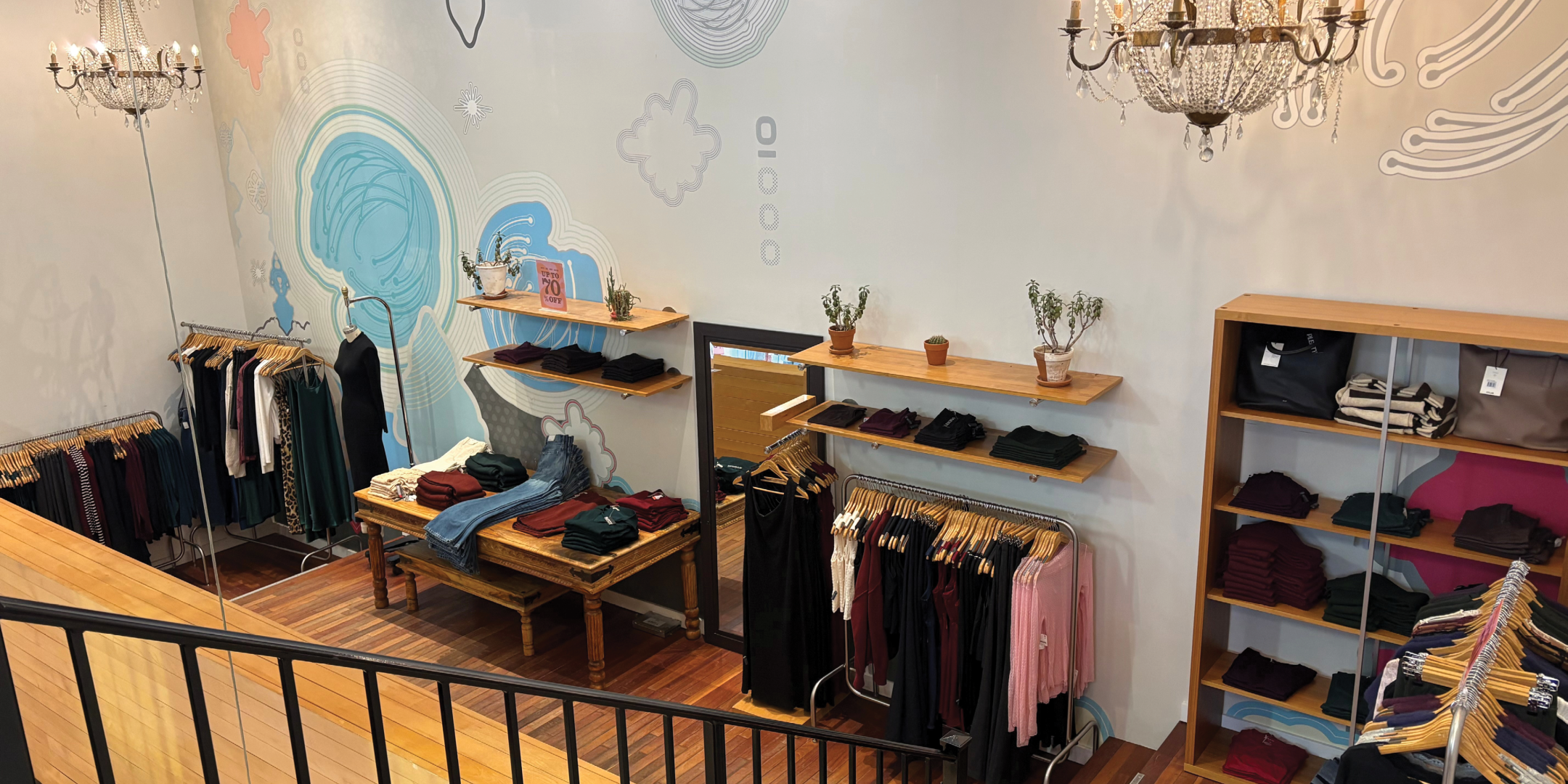 Interior of fashion retail store with clothing on racks and tables with light wood floors and white walls