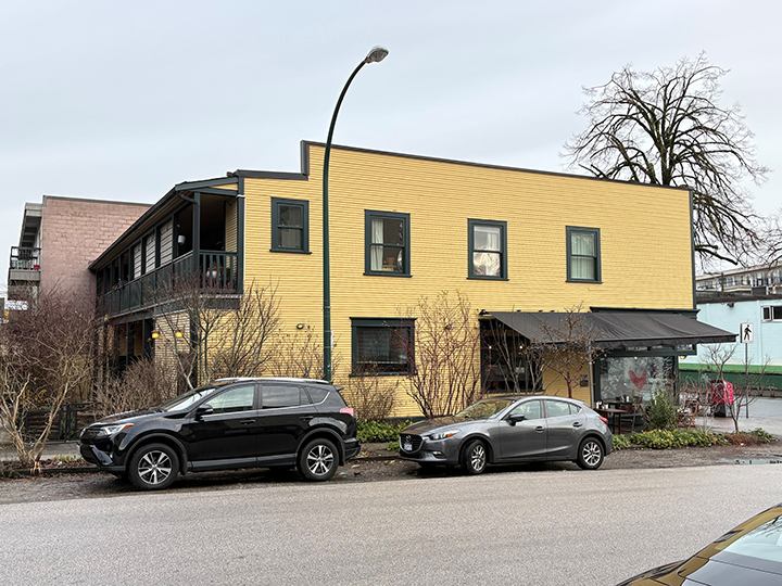 side of 2 storey mixed use commercial and residential building with yellow siding and grey accents