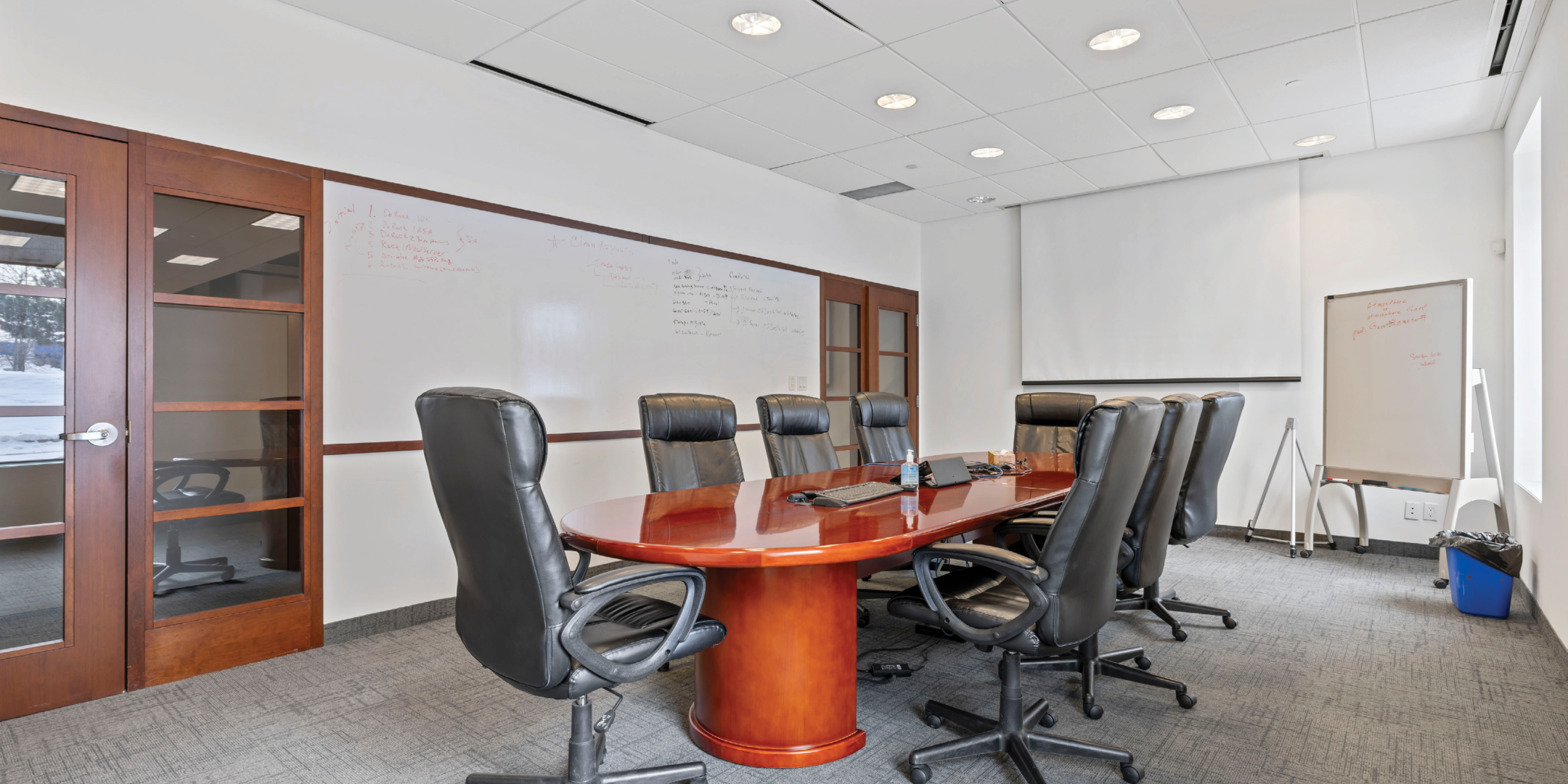 boardroom with cherrywood-coloured boardroom table with black padded chairs and white walls