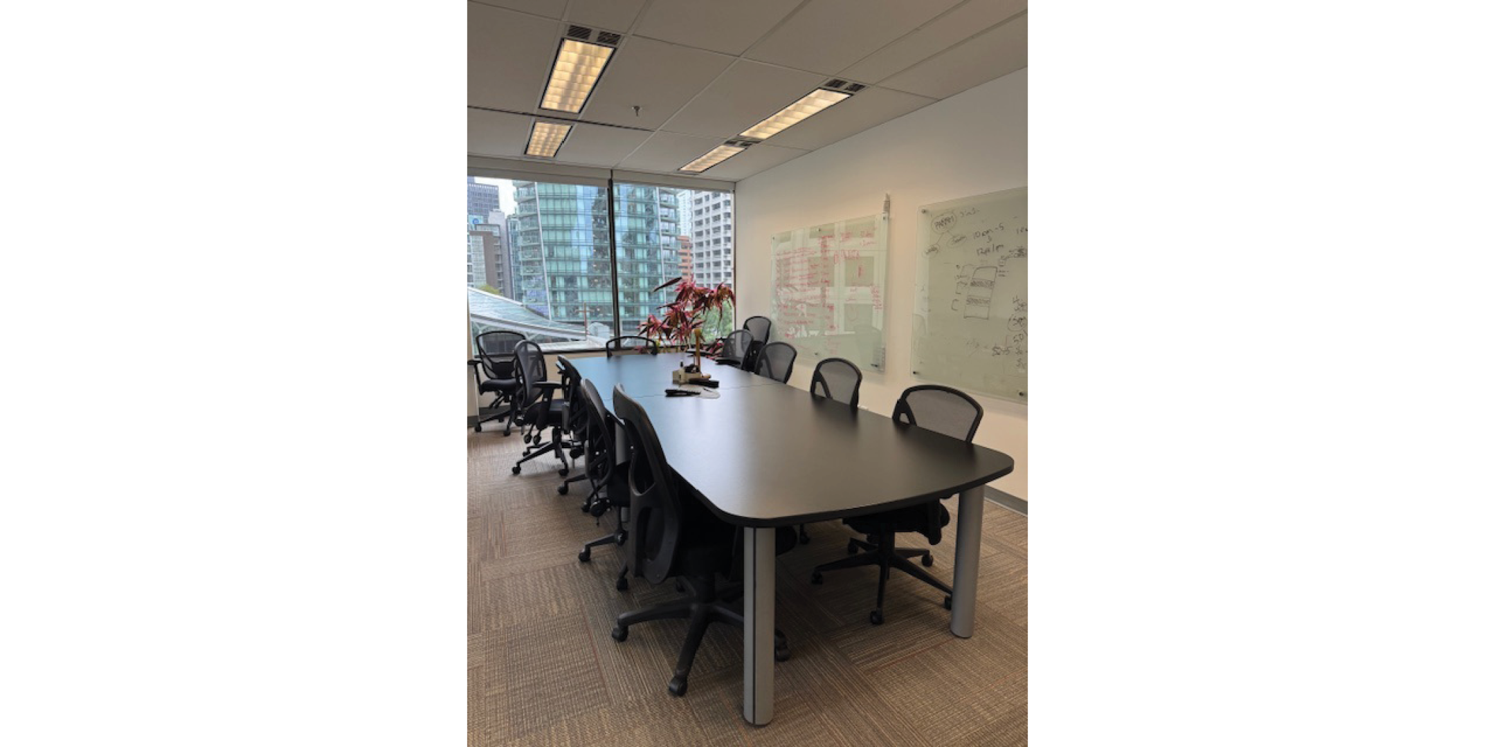 Interior of 116 Alberni Street showing a conference room with a long black table, and eight rolling chairs. Large windows show a cityscape view, and whiteboards line one wall.