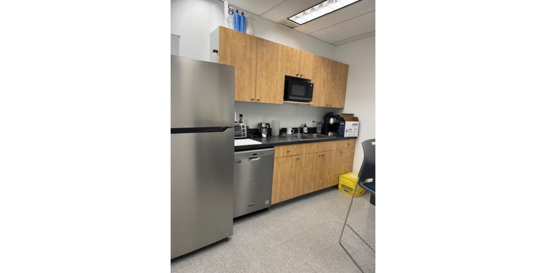 Interior of 116 Alberni Street showing an office kitchen with wooden cabinets, stainless steel fridge, microwave, and dishwasher.