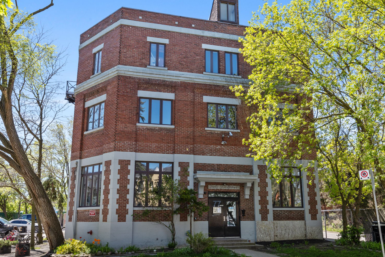 77 Florence Street exterior view of a three storey red brick commercial building surrounded by trees.