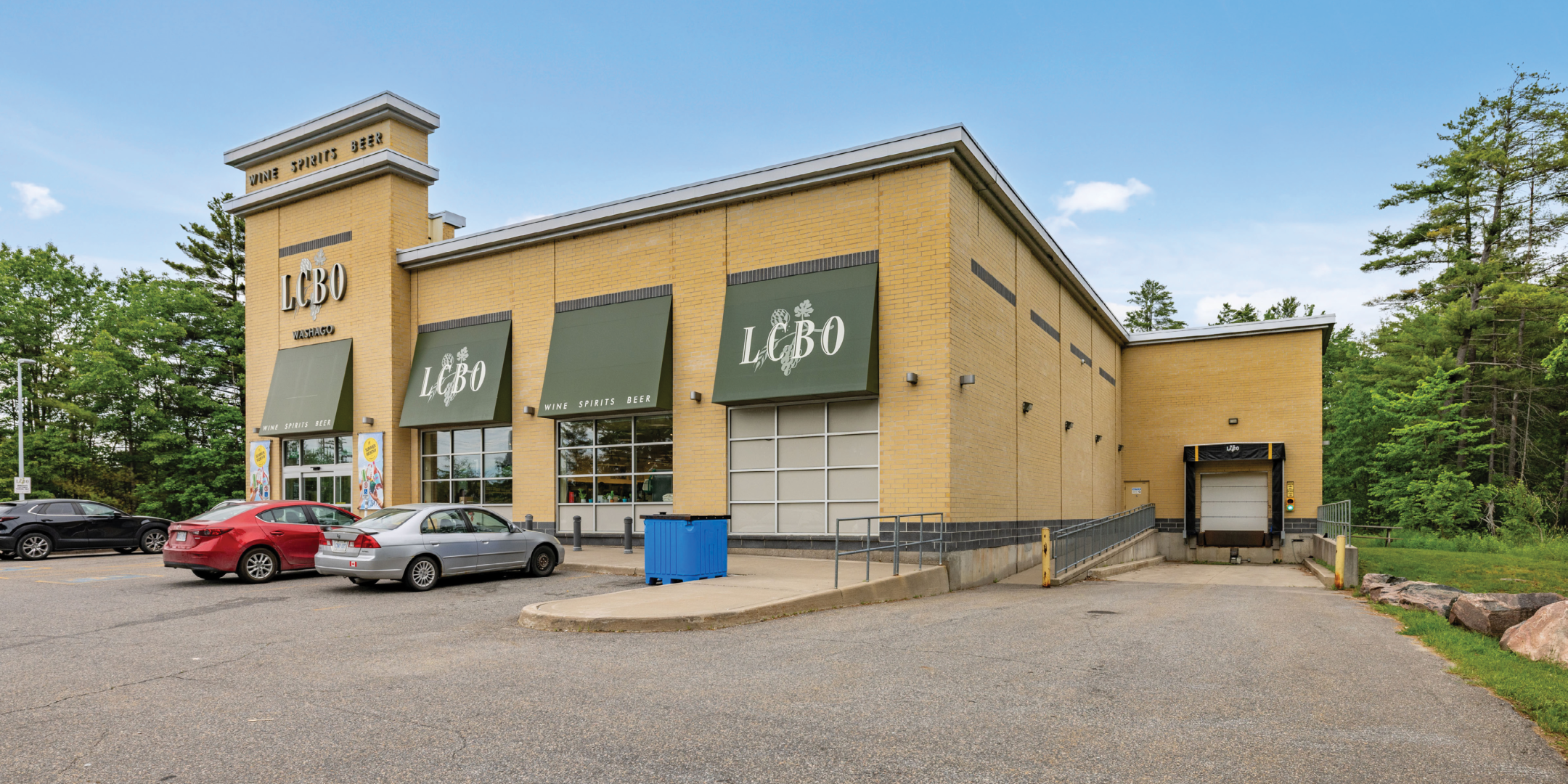 Standalone LCBO building with yellow brick with green awnings showing front and side of building including receiving door