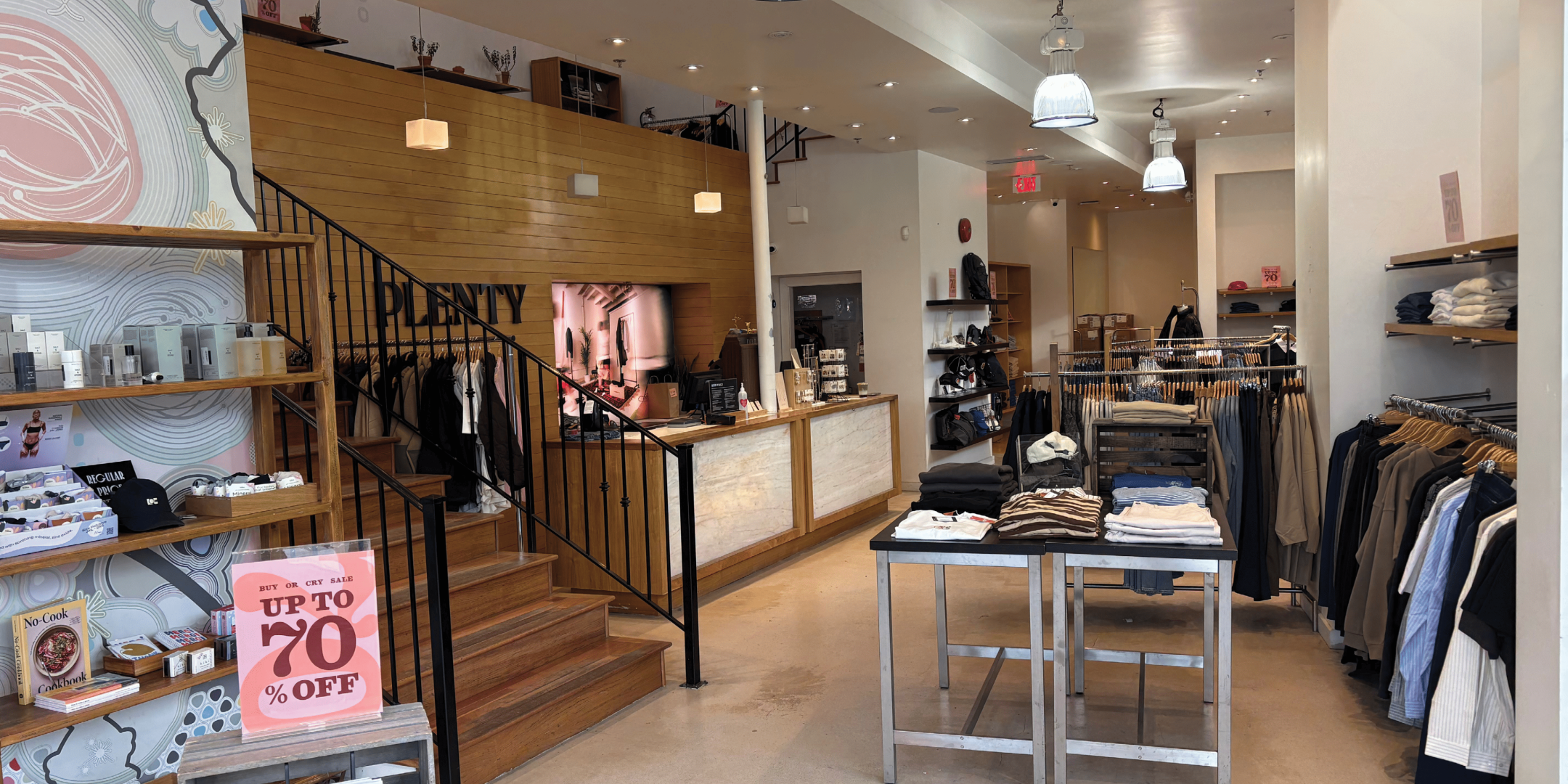 Interior of fashion retail store with clothing on racks and tables with light wood floors and white walls