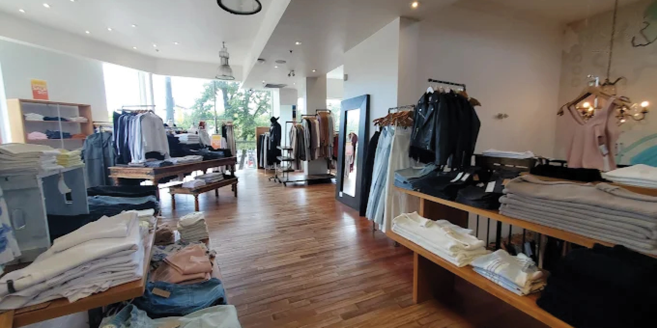 Interior of fashion retail store with clothing on racks and tables with light wood floors and white walls