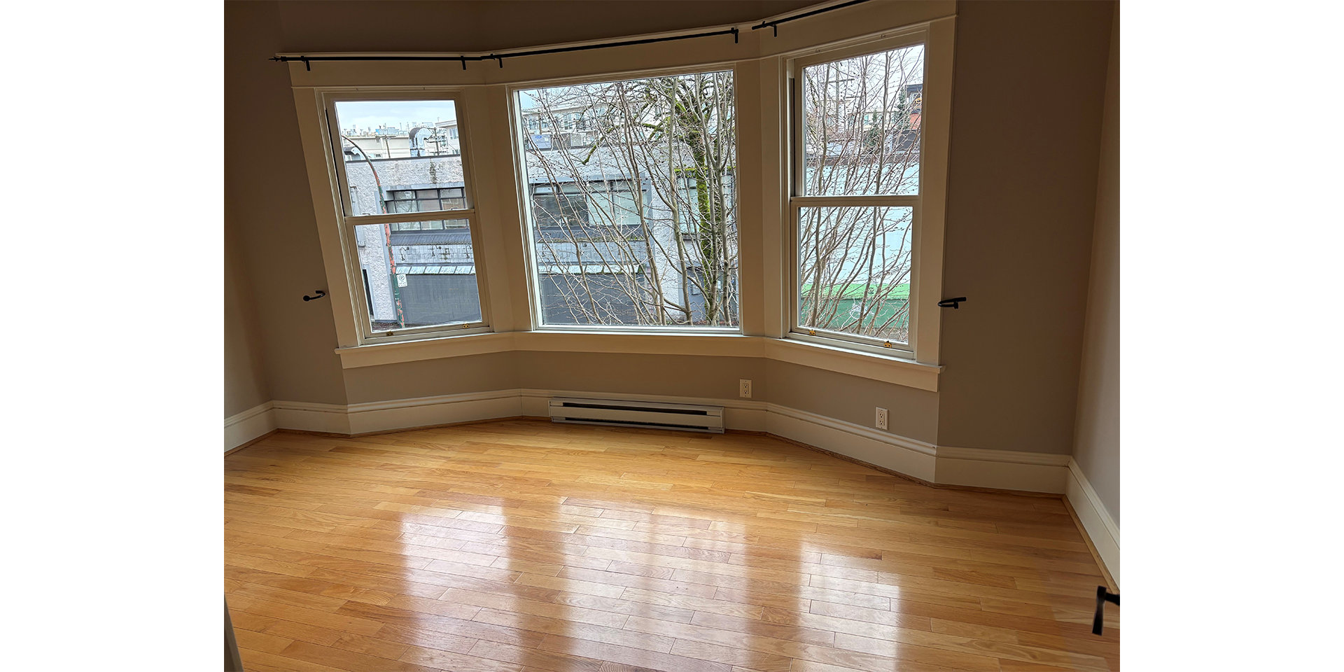 Empty room with grey walls, wood flooring, and three large windows