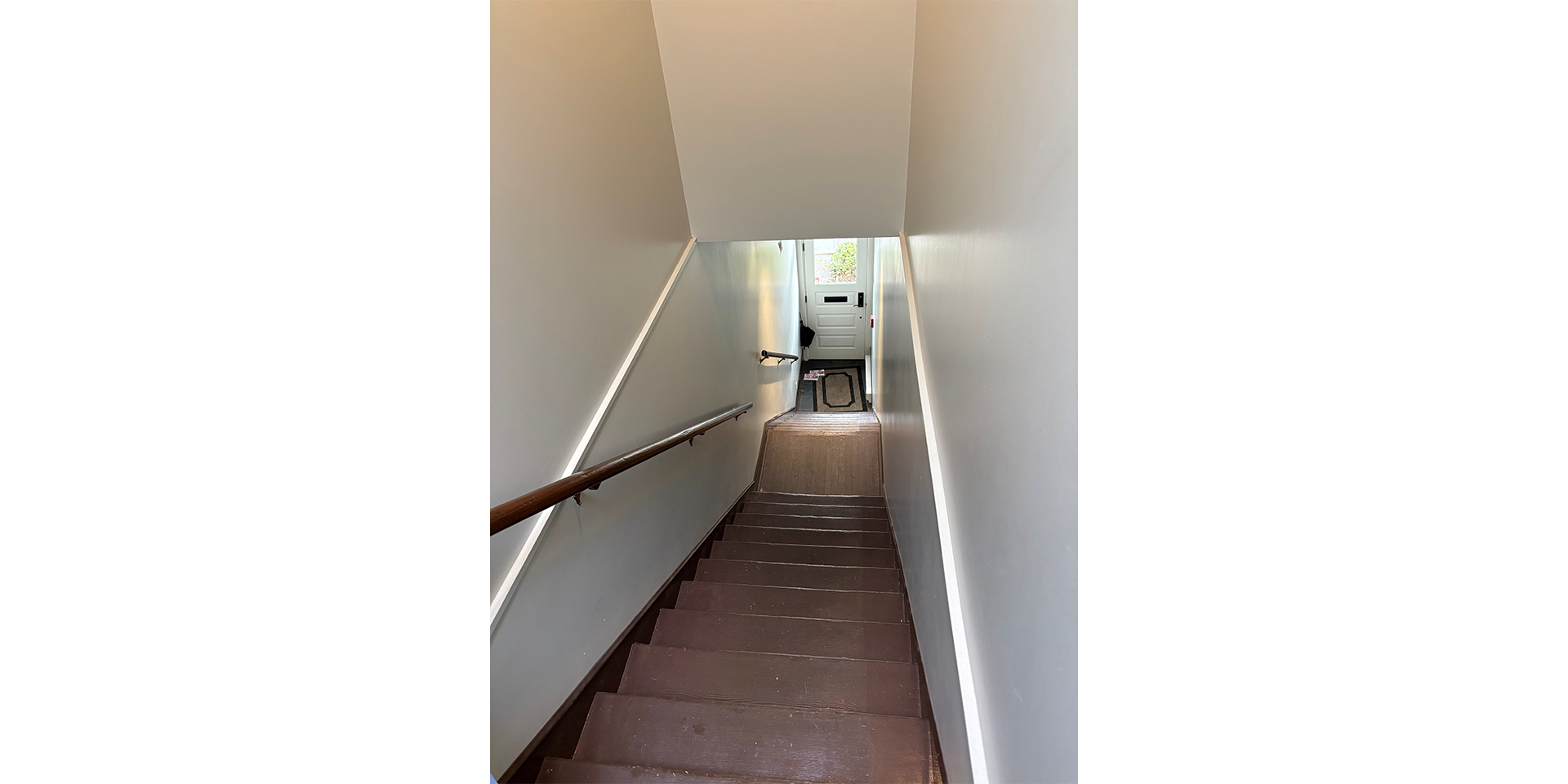 View from the top of a stairway, at the bottom is a door with a rug on the floor