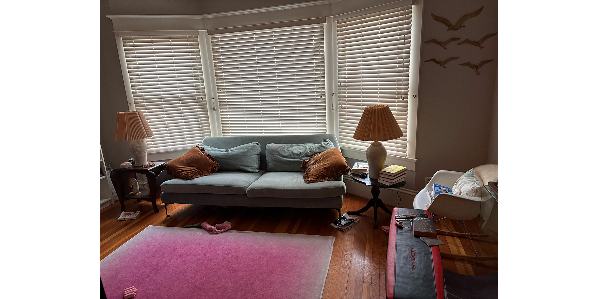Livingroom with a couch and a lamp at each side, behind the couch is a large window with blinds