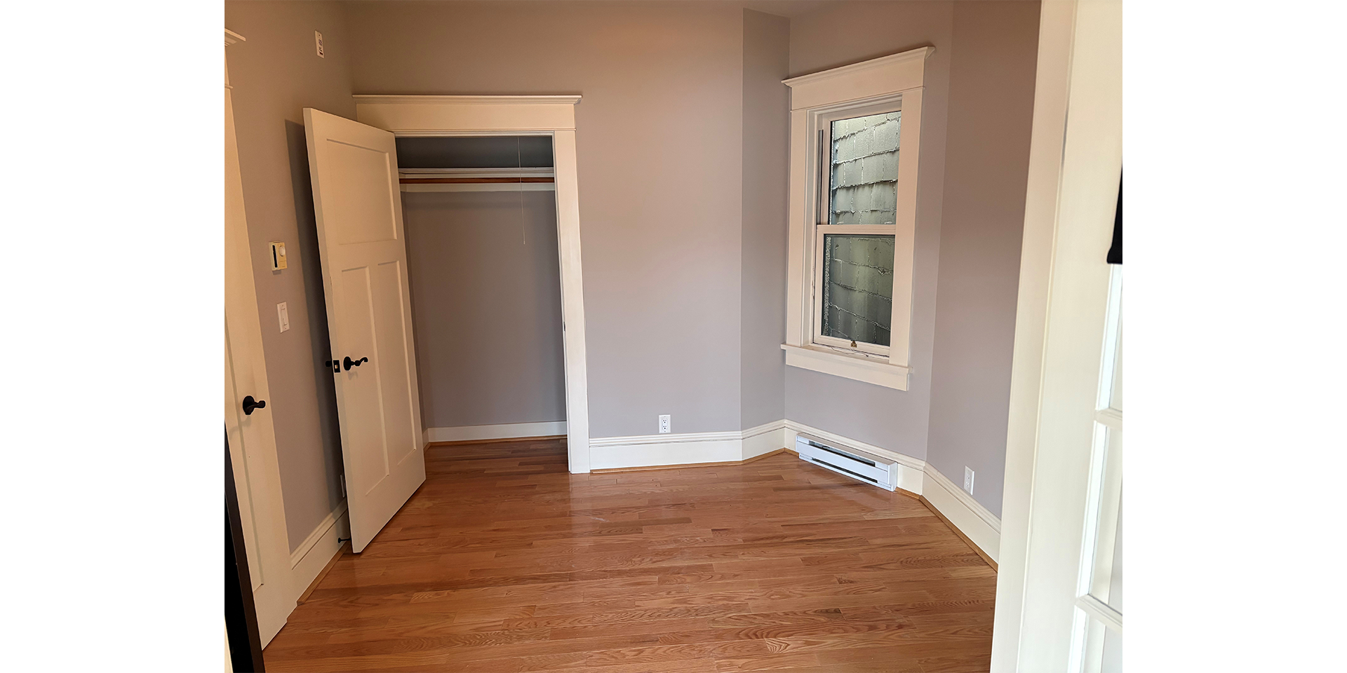 Empty room with grey walls, wood flooring, empty closet, and a small window to the right