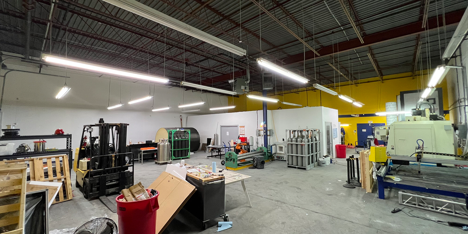 455 Cochrane Drive 24-25 warehouse features a forklift, gas cylinder storage racks, worktables, and large manufacturing machinery under bright overhead lighting.